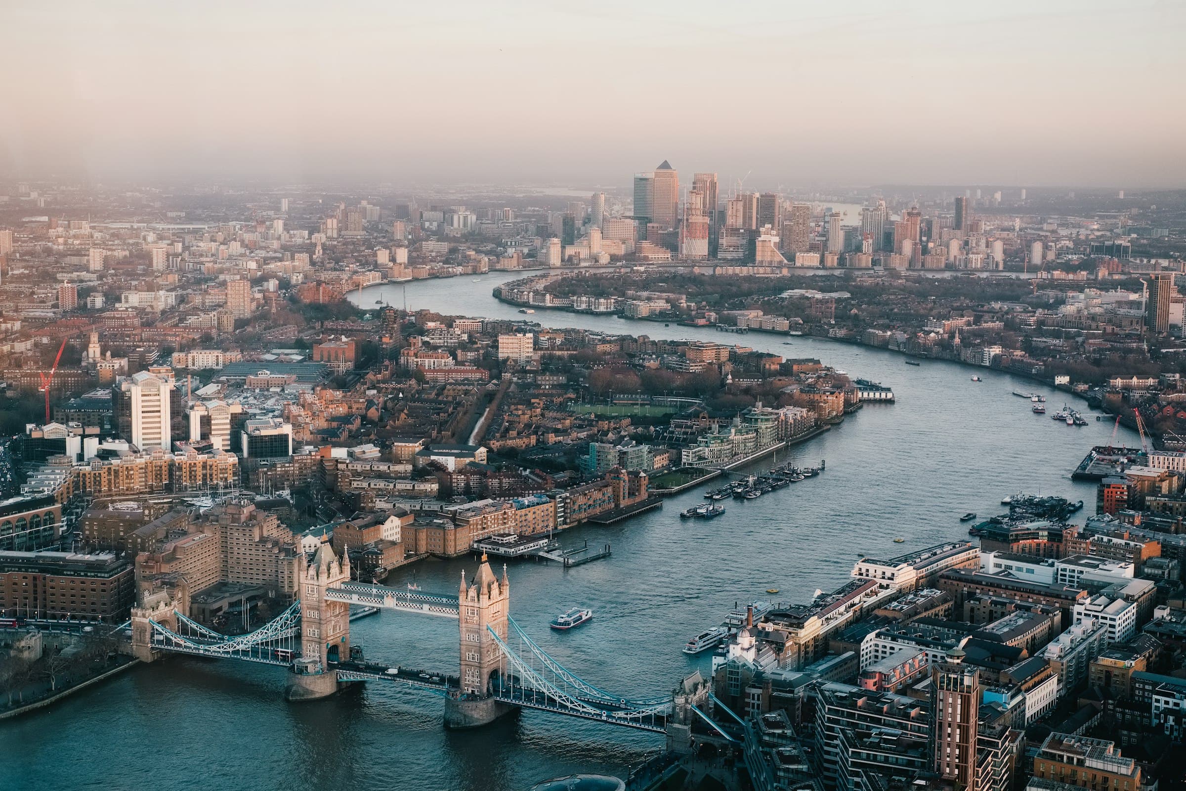 An aerial view of London at dawn, the Thames curving past Tower Bridge with Canary Wharf beyond