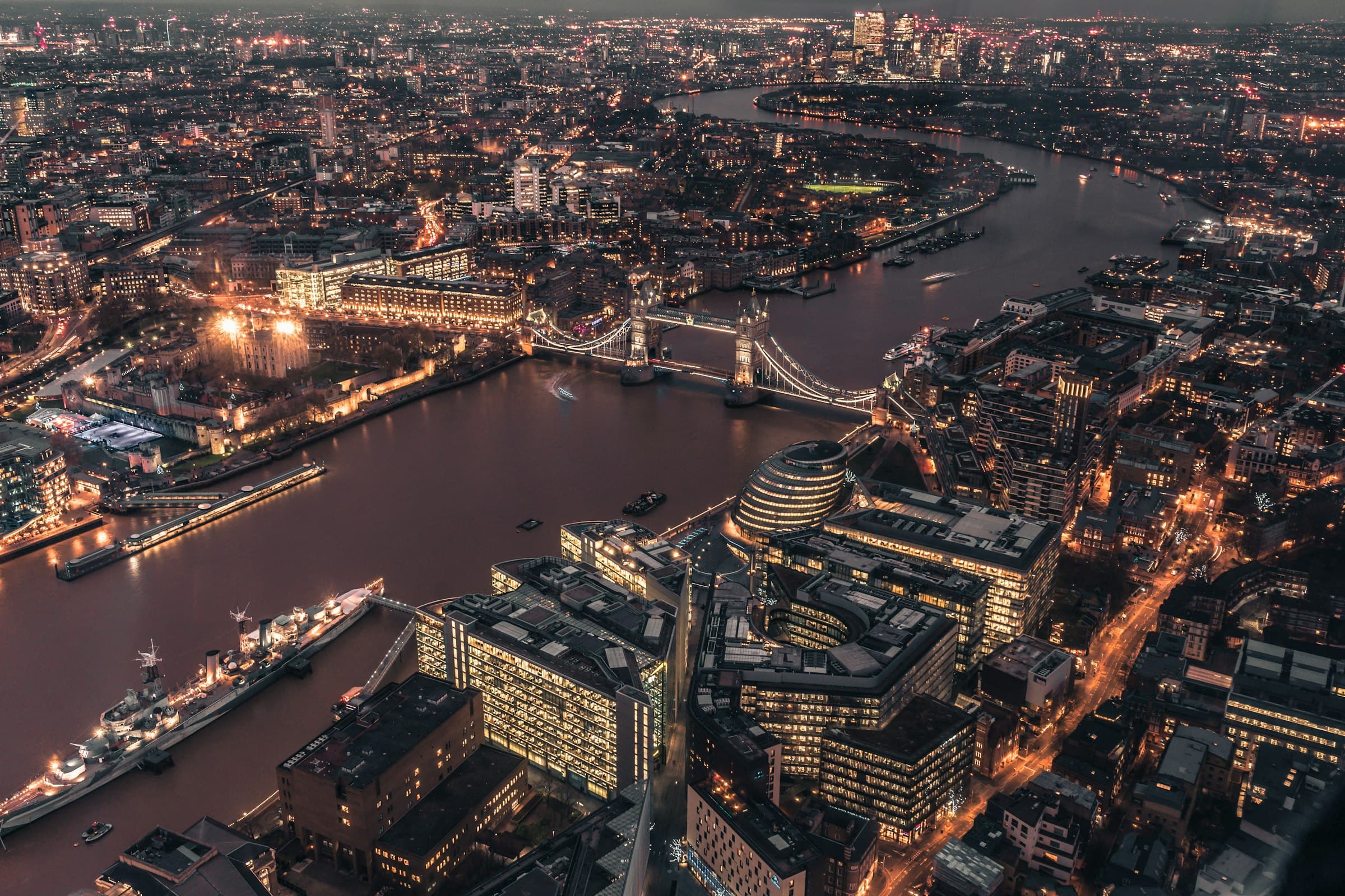 An aerial view of London at night, the Thames curving past Tower Bridge with the City lit behind